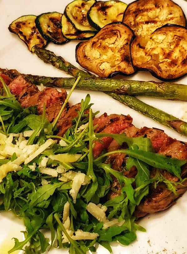 Geschnittenes Fleisch mit gegrilltem Gemüse und Rucola.